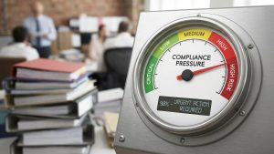A close-up of a circular industrial gauge labeled "COMPLIANCE PRESSURE" set against a blurred office background. The gauge needle points to the far right in a red "HIGH RISK" zone. A digital display at the bottom reads "98% – URGENT ACTION REQUIRED." The gauge face also features color-coded segments for "CRITICAL" (dark green), "LOW" (light green), "MEDIUM" (yellow), and "HIGH" (orange).